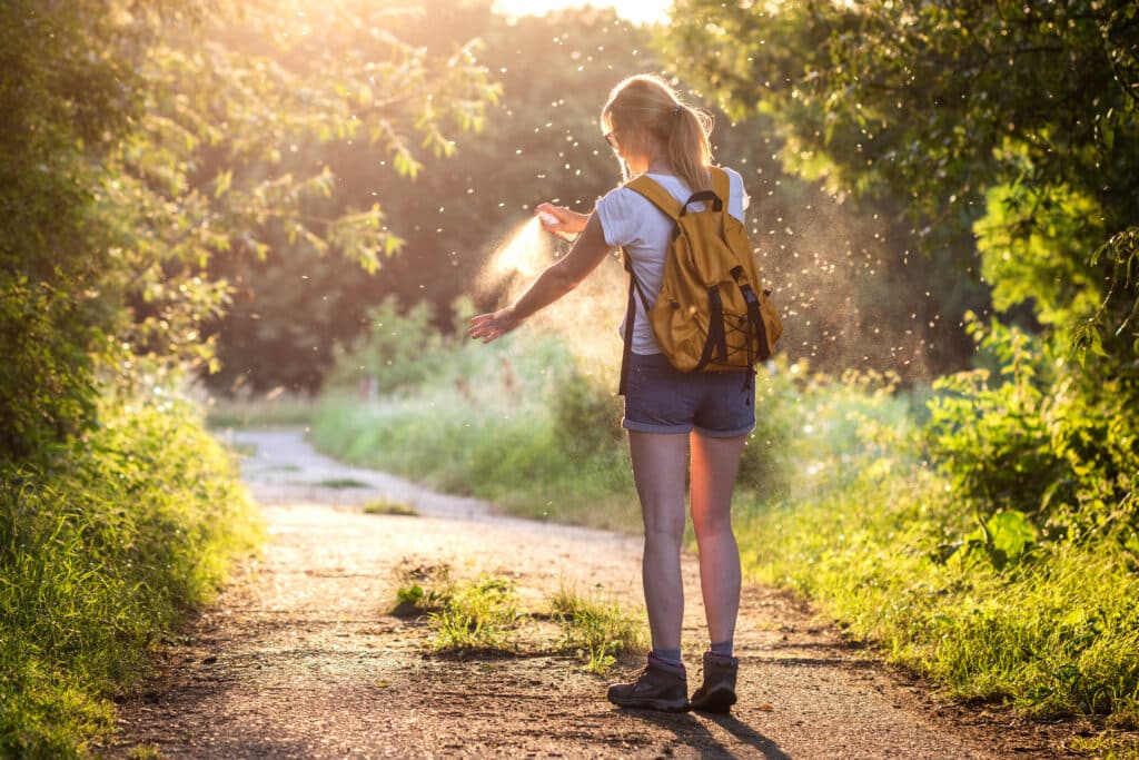 Woman surrounded by mosquitoes spraying bug spray